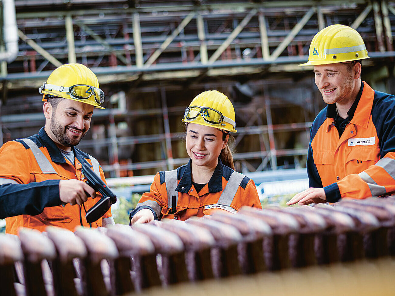Drei zusammenarbeitende Werksarbeiter, zwei Männer und eine Frau, die Arbeitskleidung, Schutzbrille sowie Helm tragen