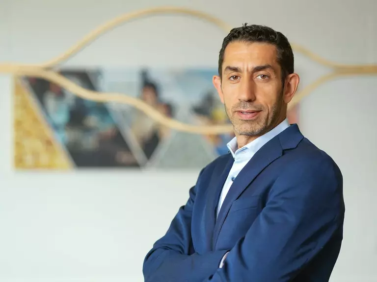 Porträt von Rakan Rahbani in blauem Anzug und hellblauem Hemd mit verschränkten Armen.