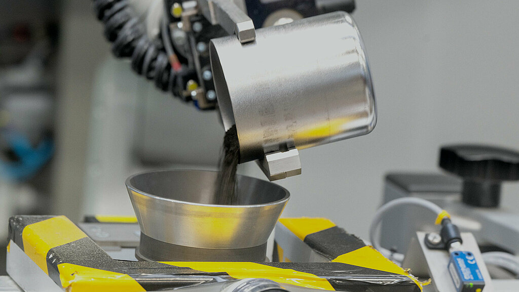 Vierte Ebene der Aurubis Performance 2030: Innovation. Zu sehen ist eine metallene Maschine, die Metallgranulat in eine Vorrichtung gießt.