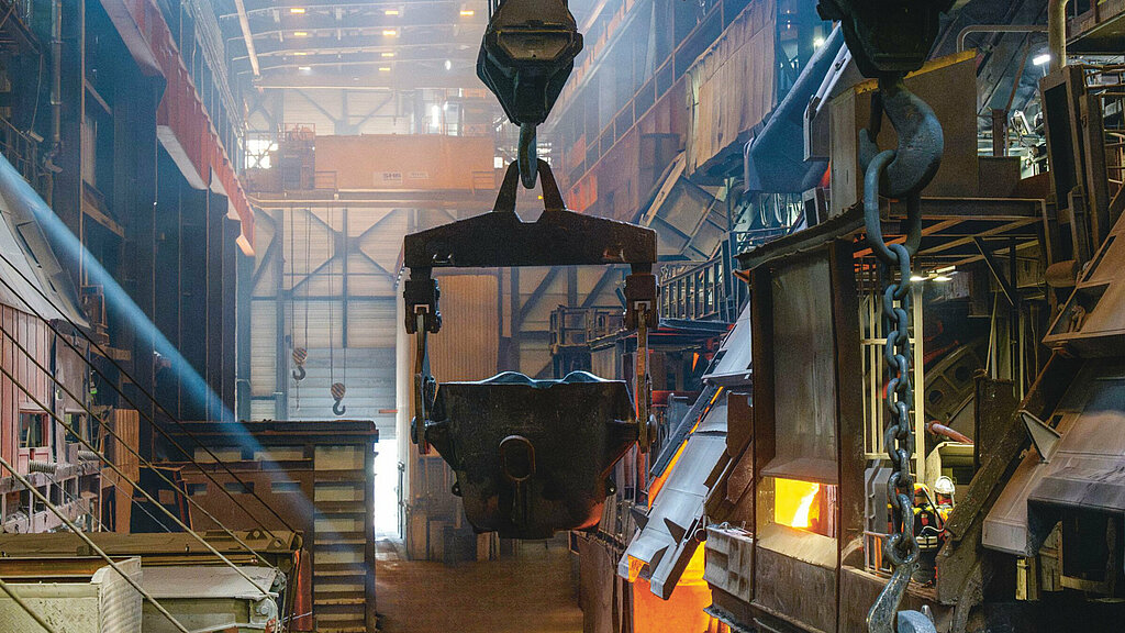 Das Innere einer Rohhütte im Aurubis Werk Ost, im Zentrum ein Kran, im Hintergrund eine Werkshalle, zur Rechten ein Schmelztiegel