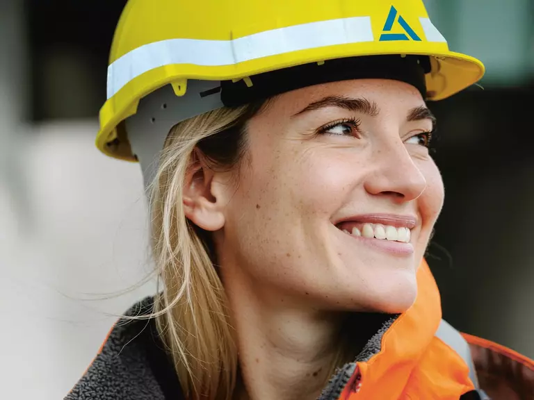 Junge Frau mit blondem Haar, orangener Warnschutzjacke und gelbem Baustellenhelm