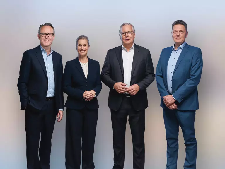 Gruppenfoto von Steffen Hoffmann (CFO), Inge Hofkens (COO), Dr. Toralf Haag (CEO), Tim Kurth (COO) im schwarzen Anzug und Kleid vor einer weißen Wand