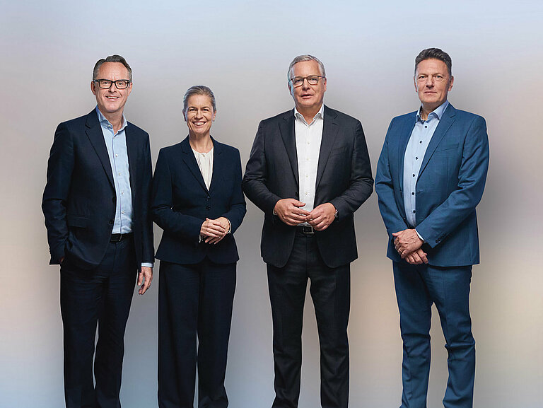 Gruppenfoto von Steffen Hoffmann (CFO), Inge Hofkens (COO), Dr. Toralf Haag (CEO), Tim Kurth (COO) im schwarzen Anzug und Kleid vor einer weißen Wand